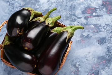 Wicker basket with fresh eggplants on blue background