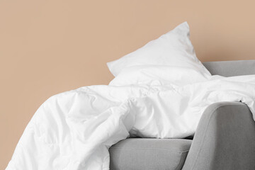 Fototapeta na wymiar Grey armchair with white blanket and pillow near beige wall