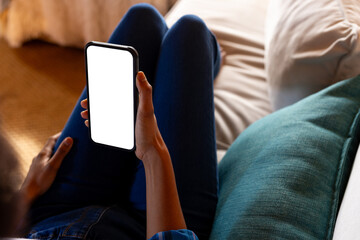 African american woman relaxing on sofa using smartphone with copy space on screen at home