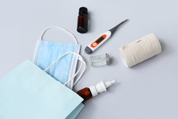 Shopping bag with medical mask, elastic bandage and thermometer on grey background