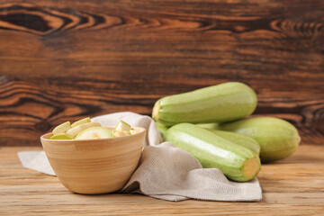 Bowl with fresh green zucchini on wooden background