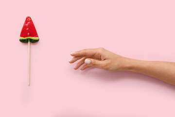 Female hand with lollipop in shape of watermelon slice on pink background