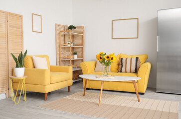 Vase with beautiful sunflowers, yellow sofa and armchair in interior of stylish living room
