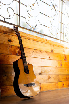Acoustic guitar leaning against wood panelled wall below window in sunny cabin, copy space