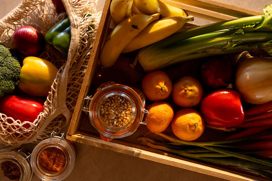 Fresh vegetables, fruit and grains in crate and re-usable shopping bag on counter in sunny kitchen