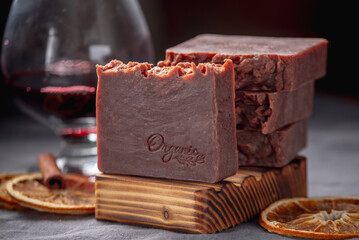 Pieces of handmade natural wine soap on a wooden soap dish, a glass of wine and pieces of orange on a grey background