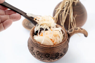 Brown clay pot with sauerkraut and wooden spoon are standing on blue cooking napkin on wooden table