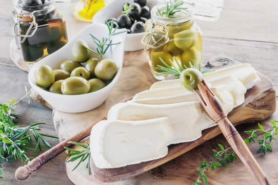 brie cheese and olives with thyme on a wooden background. Pieces of cheese on a cheese plate