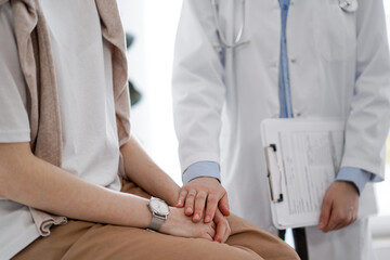 Doctor and patient discussing health exam results. Friendly physician reassuring a young woman by one hand while keeping clipboard with medical papers in another. Medicine concept