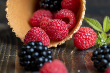 Red ripe raspberries with waffle cups on a black table