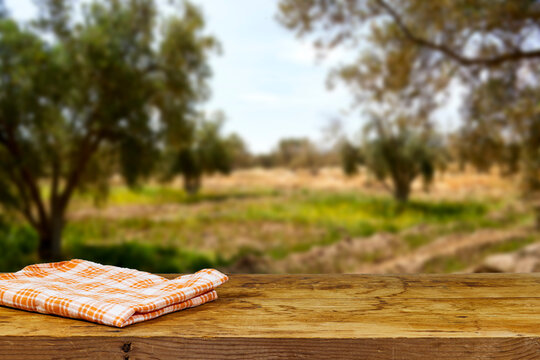 Empty wooden table with tablecloth near olives tree field