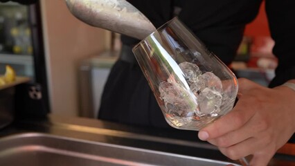Bartender girl putting ice cubes into a glass