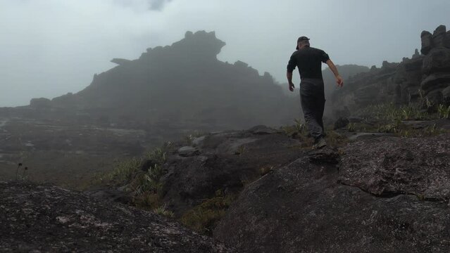 Back view of hiker walking on flat top of Mount Roraima in gloomy misty day, Canaima National Park, Venezuela