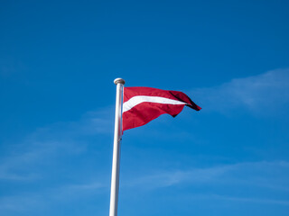 The flag of Latvia in the wind with blue cloudy sky. Exact colours of Latvian flag - carmine red with white horizontal stripe. The red-white-red Latvian flag of independent Latvia