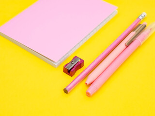 Pink office work concept, pencils, pens, markers, sharpener and notepad on a yellow background.