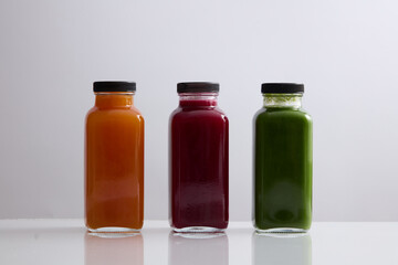 Front view of three blank label glass bottle filled with juice in orange, red and green color. Mockup design of healthy beverage brands. Organic juice concept