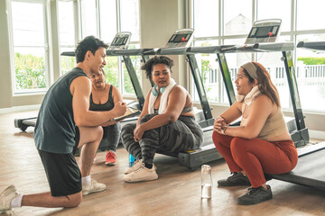 Three plus size women in sports bras sitting on treadmill having fun together and male trainer...