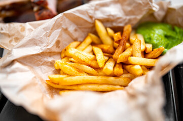 French fries lie on paper with green sauce on a wooden table. street food