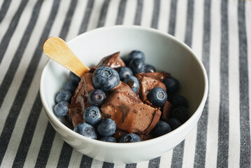 Chocolate ice cream with chocolate topping and blueberries on a striped tablecloth