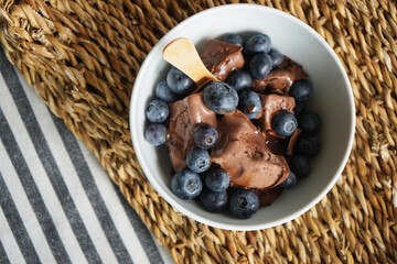 Chocolate ice cream with chocolate topping and blueberries on a sea grass stand on a striped tablecloth