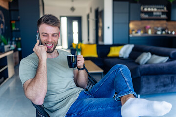 A good-looking man sits in a chair after a busy day, drinks coffee and talks on the phone with his partner