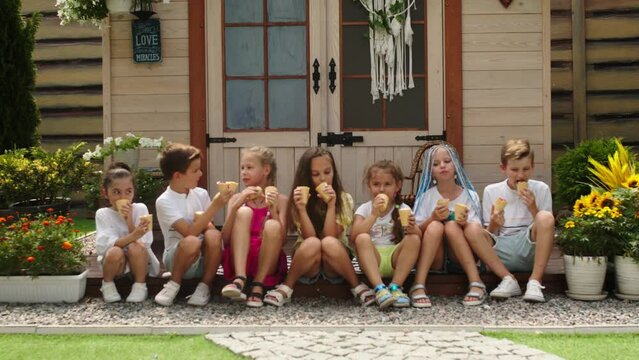 A group of small children of different races eat ice cream and enjoy a warm summer day on the terrace. Advertising happy children and healthy food.
