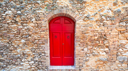 Fototapeta na wymiar Antique wooden door, vibrant red paint, historic walls, San Gimignano, Tuscany.