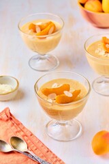 Dessert, mousse or panna cotta with apricots and almond petals in transparent bowls on a light concrete background. Summer desserts, fruit mousses and jellies.