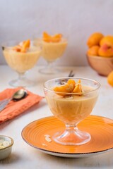 Dessert, mousse or panna cotta with apricots and almond petals in transparent bowls on a light concrete background. Summer desserts, fruit mousses and jellies.