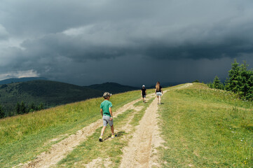 Fototapeta premium Mom with children walks in the mountains on the eve of a thunderstorm. People go down from the mountain to a safe place