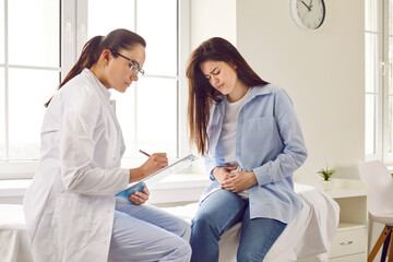 Obraz premium Young woman suffering from stomach ache having consultation with doctor in medical office. Female patient visiting gynecologist, gastroenterologist, therapist or GP in medical clinic