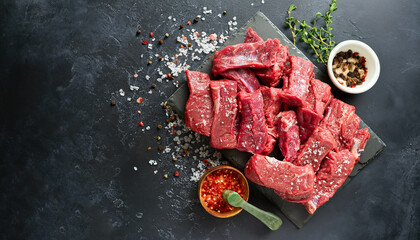Cut beef into small pieces with sea salt, dried herbs and chili peppers on dark slate or concrete...