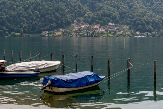 Covered boats anchored on the lakefront of Caslano, Switzerland, with Carabietta in the background
