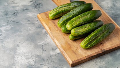 Crispy cucumbers on a wooden stand. Fresh green vegetables, organic farmer product. Wooden chopping board, marble stone background, copy space