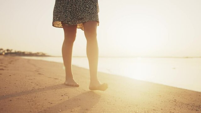 Barefooted legs of woman tourist barefooted feet walking on sandy ocean beach leaving footprints in luxury resort at sunset outdoors. Female enjoying resting on summer vacation. Travel, tourism.