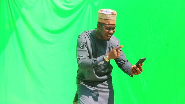 Hausa tribe man of northern Nigeria in Africa celebrates win seen of phone and shows camera the phone screen