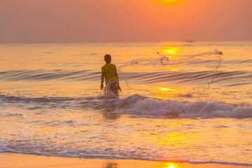 A young Fisherman throwing a net to the sea at sunrise in Thailand.