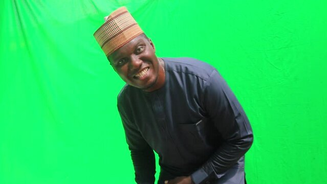 Happy African business man in Hausa cap bends over, comes close to camera and waves to the viewers