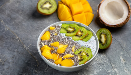 Mango smoothie bowl with pieces of kiwi, mango, coconut shavings and chia seeds on a stone...
