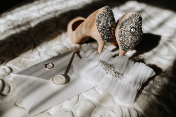 wedding shoes of the bride on a high heel of beige color with stones above the heel, an envelope with a wedding vow and a wedding ring of the bride is standing next to it