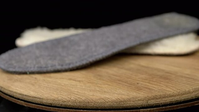 Close up, Warm Woolen Shoe Insoles Rotate on a Wooden Board, Black Background. Side view. Two. Blurred motion. Selective focus. Spinning by circle. Copy space. Isolated. Wintertime. Orthopedic.