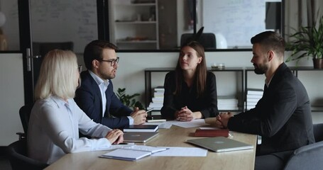 Serious confident young business partners talking on team meeting, negotiating on deal, contract, getting happy, positive, shaking hands over table. Employer hiring candidate after job interview