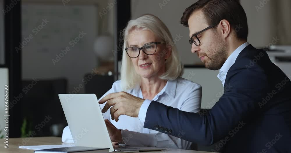 Poster confident business man presenting project to mature older colleague, pointing at laptop display, tel