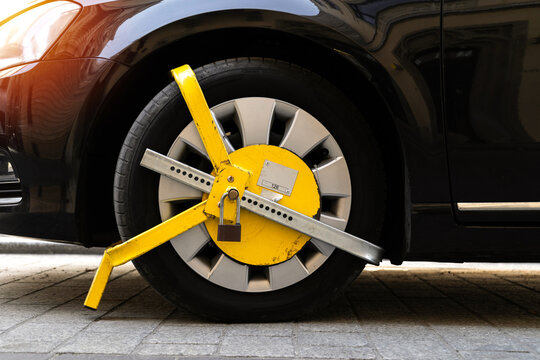 Car wheel blocked by a yellow metal lock or clamp. Vehicle illegal parking violation in a restricted zone.