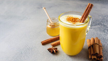 Turmeric golden milk latte with cinnamon sticks and honey. Healthy ayurvedic drink. Trendy Asian...