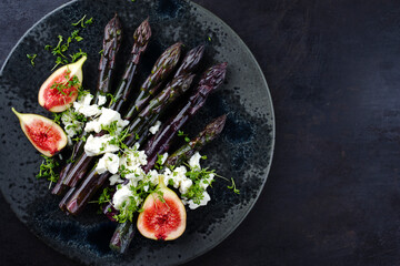 Traditional glazed purple asparagus with feta cheese and figs served as top view on a Nordic design plate with copy space right