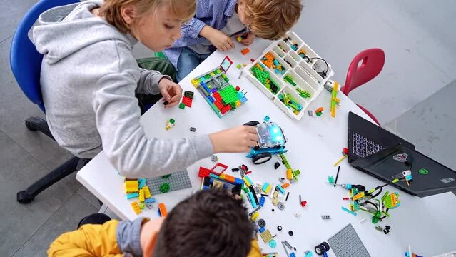 Robotics programming class. Children construct and code Robot. STEM education using constructor blocks and laptop tablet, remote control joystick. Technology educational development for school kids