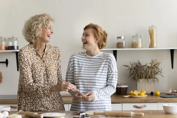 Fotobehang Joyful excited mom and adult daughter baking sweet homemade pastry snacks, cookies, biscuits, shaping, rolling dough, talking, discussing family recipe, smiling, laughing, having fun © fizkes
