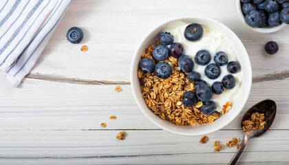 Yogurt. Greek Yogurt with granola and fresh blueberries in white bowl over old white wood background. Morning breakfast concept. Healthy food for breakfast, top view