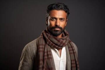 Fototapeta premium Portrait of a handsome bearded Indian man wearing a scarf over grey background